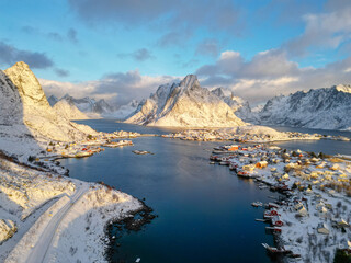 Aerial view of Lofoten island Norway. The winter season of sunrise fishing village of Reine with snowscape mountain peak reflect on water. Norway with red rorbu houses. With falling snow in winter.