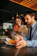 A diverse couple snapping pictures of their dishes and each other in a cozy cafe setting