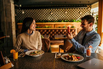 A man and a woman capturing moments and meals with their phones at a local diner