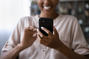 Happy African American young woman using app on mobile phone, reading funny text message, laughing,...