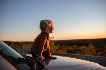 Child sitting on car at overlook watching autumn sunset