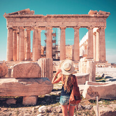 Travel destination in Athens- Young woman tourist with hat and bag looking at old ruin temple,...