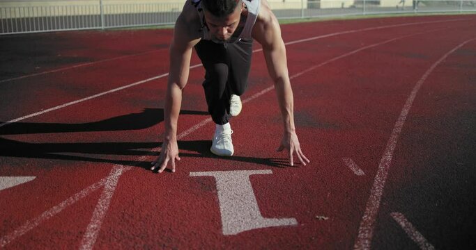 Young african american man doing star pose at starting point before running exercise on track in sport stadium