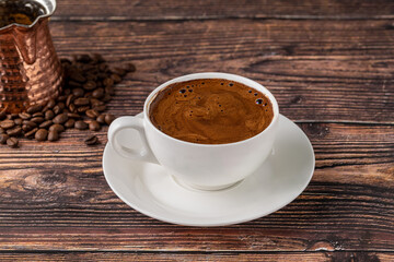 Double Turkish coffee in a white porcelain cup with a decorative coffee pot on a wooden table