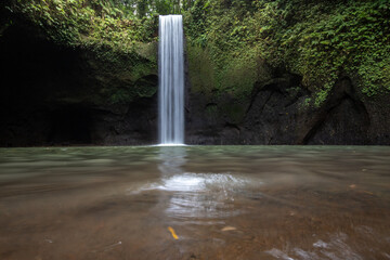 Tibumana Waterfall a small wide waterfall in a green gorge. The river falls into a basin in the...