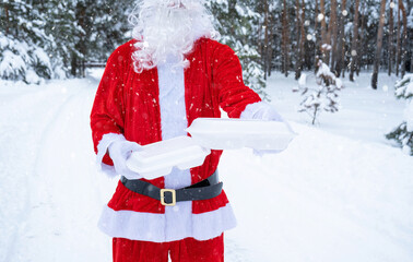 Food delivery service containers in hands of Santa Claus outdoor in snow. Christmas eve promotion. Ready-made hot order, disposable plastic box. New year holidays catering. Copy space, mock up