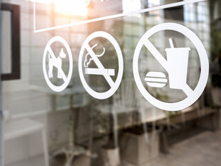 Close-up of no food and drink icon, pet and no smoking forbidden sign, white sticker on glass front...
