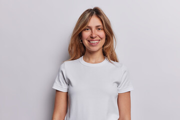 Waist up shot of pleasant looking woman with piercing in nose dressed in casual t shirt keeps arms...