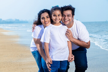 Happy indian Family of three enjoying summer vacation. Man and woman posing for photograph with their daughter on beach.