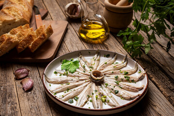 Rustic dish with anchovies in vinegar and seasoned with garlic and parsley, along with some slices of bread on an old wooden table.