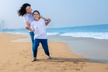 Happy YOUNG indian Mother and daughter playing at beach, Summer holidays and vacation. Copy space. 