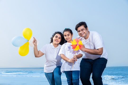 Happy indian Family enjoying summer beach holidays vacations. parents with their daughter hold balloons pin-wheel. 