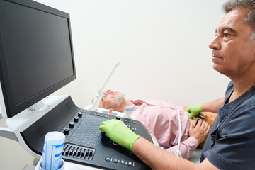 Experienced diagnostician conducts an ultrasound examination on patient - obrazy, fototapety, plakaty