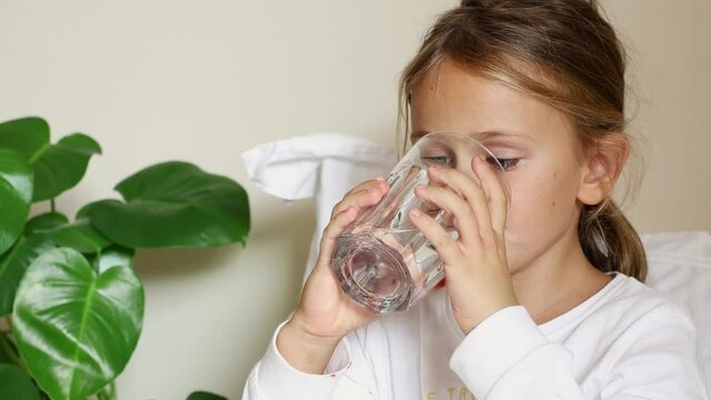 Health stay hydrated concept. Thirsty Child Drinking Water at home in pajamas. Kid drink fresh pure water glass cup get sick on bed. Take care body. Morning routing. Hydration tips for children