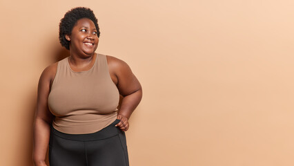 Horizontal shot of positive curly haired African woman has excess weight dressed in t shirt and...