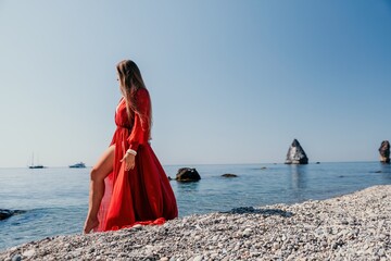 Fototapeta na wymiar Woman travel sea. Happy tourist in red dress enjoy taking picture outdoors for memories. Woman traveler posing on the rock at sea bay surrounded by volcanic mountains, sharing travel adventure journey