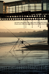 A fishing rod left out underneath a pier at sunset by the sea