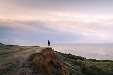 A man looks out to sea at sunrise on the top of a cliff edge