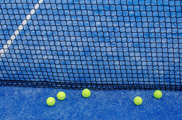blue paddle tennis court net with five balls nearby, racket sports concept