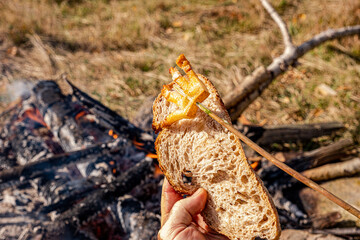 a man hand holds a slice of toasted bread with fried bacon an open fire in nature, slanina,traditional food in Romania