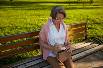 Old woman taking pills from bag after feeling bad on walk in park
