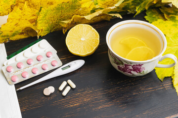 Capsules, pills, medicine in a blister pack, thermometer, tea cup with lemon on a wooden table with...