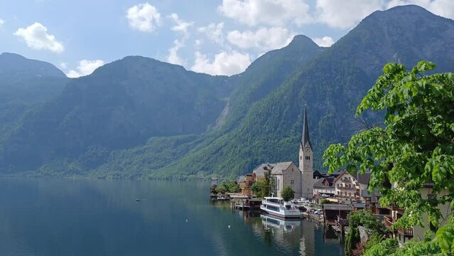 Beautiful view of Hallstatt town with Hallstatt lake, boat, church tower and Apls mountain in background.