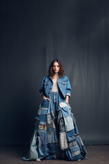Famale model wearing an avant-garde, eco-friendly outfit composed entirely of recycled denim dress with various shades of blue denim pieced together in an artistic patchwork