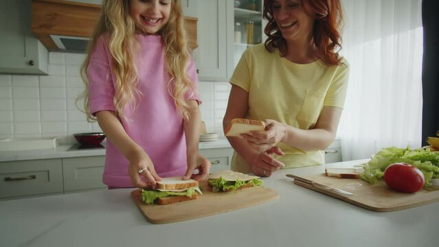 Friendly and smiling mother with daughter in the kitchen are folding sandwiches and hugging warmly. Showing a high five gesture for a job well done. The concept of happy motherhood and childhood.