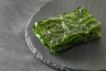 Nori sheets of dried green algae, on slate stone plate round, dark background, selective focus.