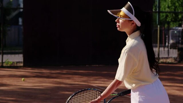 A young girl athlete throws up the ball for serving to opponent and strikes with a racket in a practice tennis match. A lady sportswoman is training and preparing for international competitions or