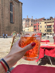 hand holds glass of local Italian cocktail Aperol spritz over city in Italy