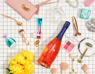 Top view of champagne bottle, yellow flowers and decorative cosmetic. Eye shadow for fashion makeup, roller facial massagers, makeup brushes. 
