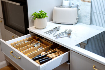 Organizing silver cutlery and kitchenware in kitchen drawer. Storage organization system in kitchen 