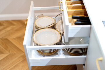 Open kitchen drawers with dishware and cutlery neatly organized. Storage organization system in...