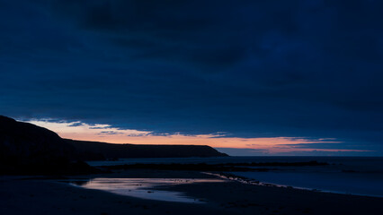 Fototapeta premium Beautiful sunrise landscape image of Kennack Sands in Cornwall UK wuth dramatic moody clouds and vibrant sunburst