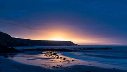 Beautiful sunrise landscape image of Kennack Sands in Cornwall UK wuth dramatic moody clouds and vibrant sunburst