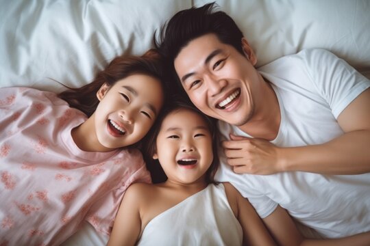 Portrait of Asian family lying on bed. Top view of mom, dad and child.