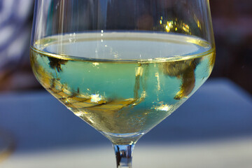 Glass of wine on the beach, mirroring the blue of the sky and a beige curtain