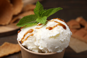 Scoops of tasty ice cream with caramel sauce and mint leaves on blurred background, closeup