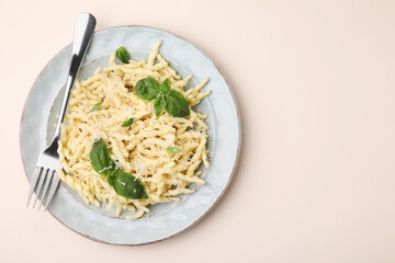 Plate of delicious trofie pasta with cheese, basil leaves and fork on beige background, top view. Space for text