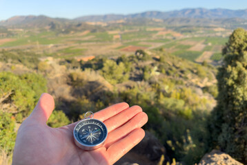 Compass in hand in mountains. Tourist compass for orientation on terrain. Magnetic declination...