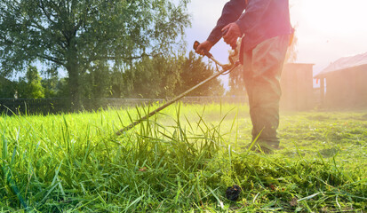 Gardener mows weeds grass. Man cutting grass in yard by using string trimmer. Worker lawn mower...