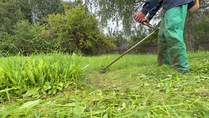 Gardener mows weeds grass. Man cutting grass in yard by using string trimmer. Worker lawn mower cutting green garden. Lawn mowing machine. Grass Trimmer and Grass Cutter. lawn maintenance service.