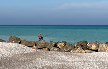 Fototapeta na wymiar Fisherman catches fish on coast near sea. Catching fish in sea from shore. Fishing by sea. Catching fish on spinning at ocean from shore.
