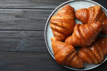 Delicious fresh croissants on black wooden table, top view. Space for text