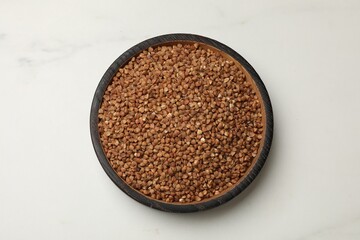 Bowl with dry buckwheat on white marble table, top view