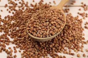 Spoon with dry buckwheat on light wooden table, closeup