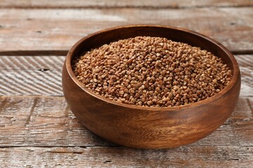 Bowl with dry buckwheat on wooden table, closeup