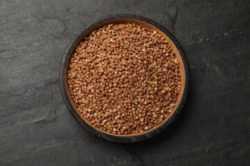 Bowl with dry buckwheat on black table, top view